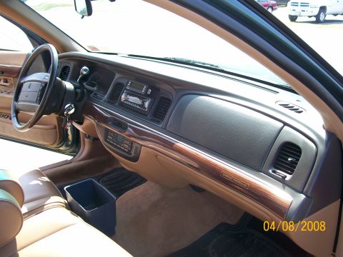 1995 Mercury Grand Marquis - Interior of a 1990s Mercury Grand Marquis shot from the open passenger door, showing the tan-and-gray dash with woodgrain trim, a 'Grand Ma…