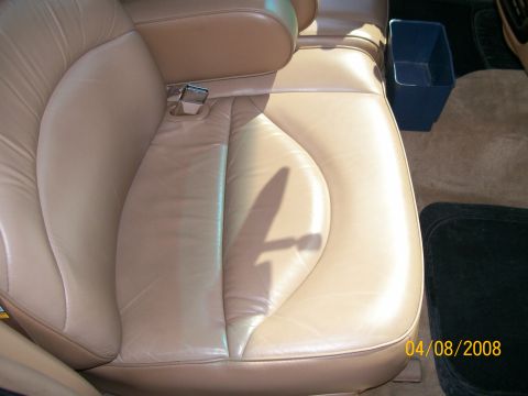 1995 Mercury Grand Marquis - Close-up of a tan leather front bucket seat cushion and bolster with a chrome seat belt buckle receiver rising from the inboard side, photo…