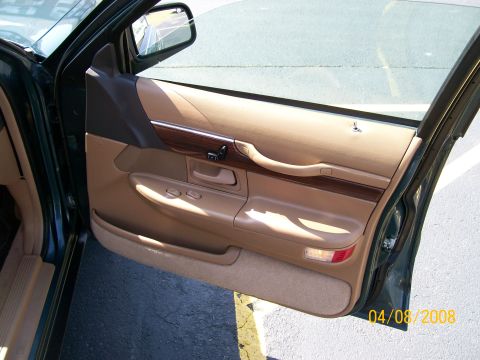 1995 Mercury Grand Marquis - Open passenger door of a dark green sedan showing the tan door panel with woodgrain insert trim, chrome accent strip, power window and lock…