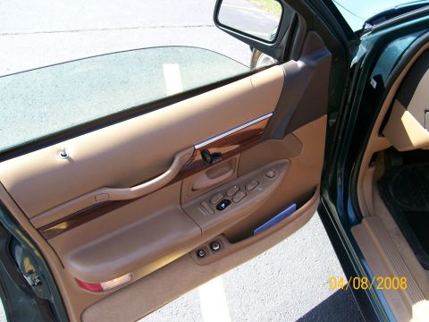 1995 Mercury Grand Marquis - Inside face of an open front door on a green sedan, showing the tan door panel with wood-grain accent strip, chrome pull handle, power wind…