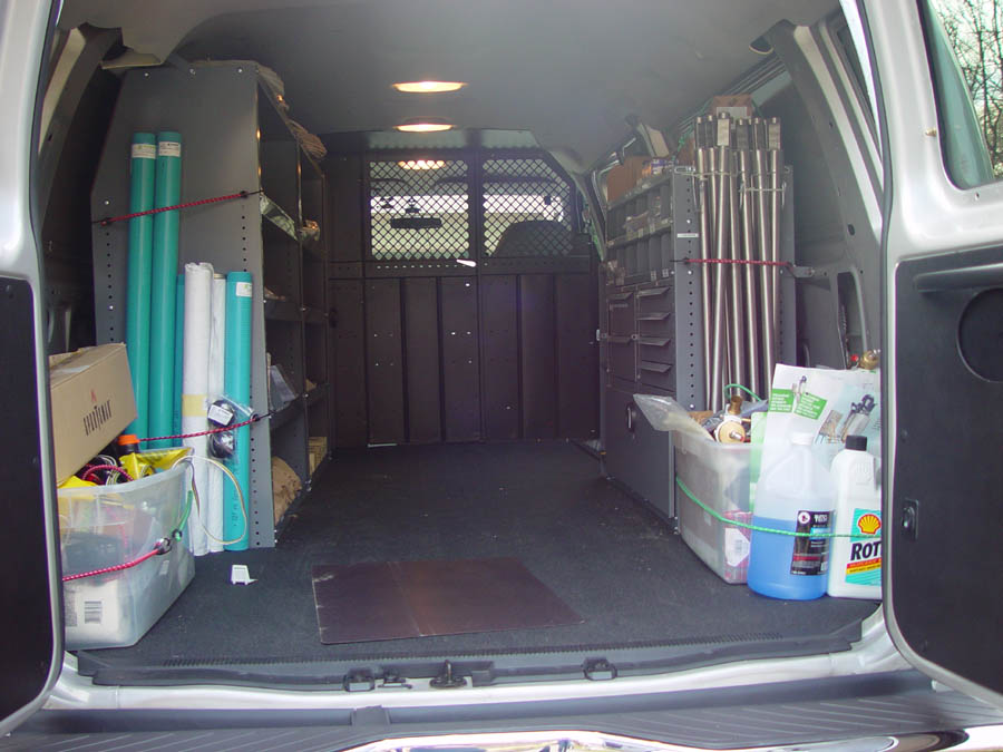 Rear cargo interior of a work van with shelving, rolled materials, bins and oil jugs