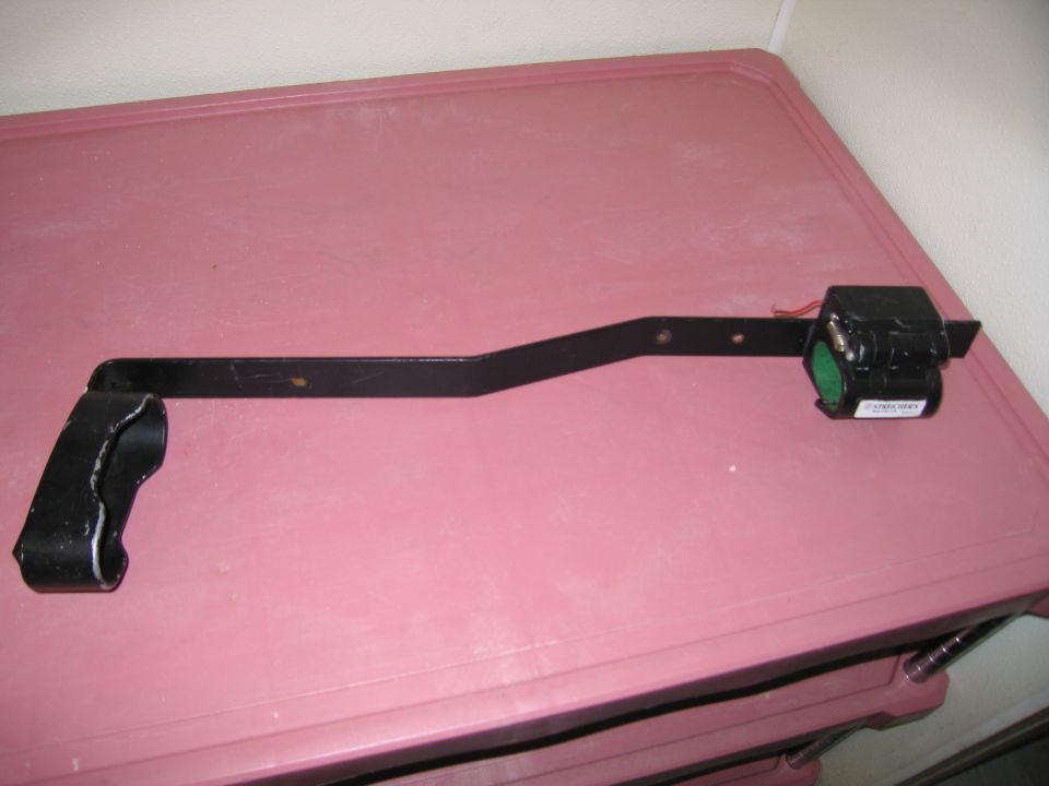 Black metal bracket with a black electrical component attached, showing a green circular part and a white label with text
