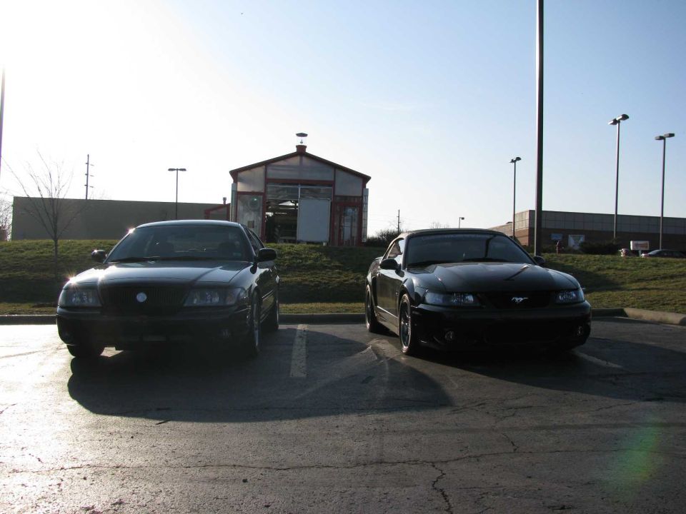 Two black cars, one looks like a Ford Mustang, parked outside a building