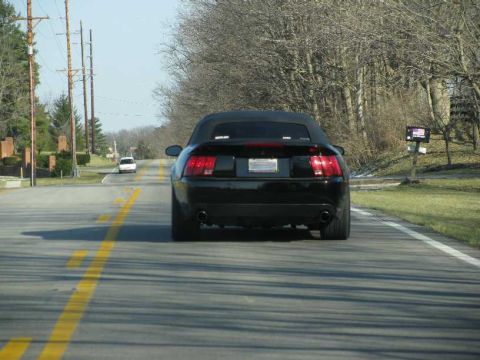 2003 Mercury Marauder - A black convertible sedan is seen from behind on a two-lane road with a white car ahead.