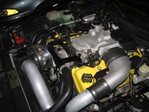 2003 Mercury Marauder - Close-up view of a modified engine bay a prominent supercharger and yellow painted valve covers.