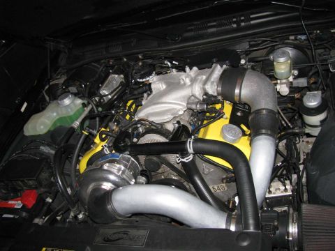 2003 Mercury Marauder - Engine bay a supercharger and yellow valve covers. Some text is visible on the engine block.