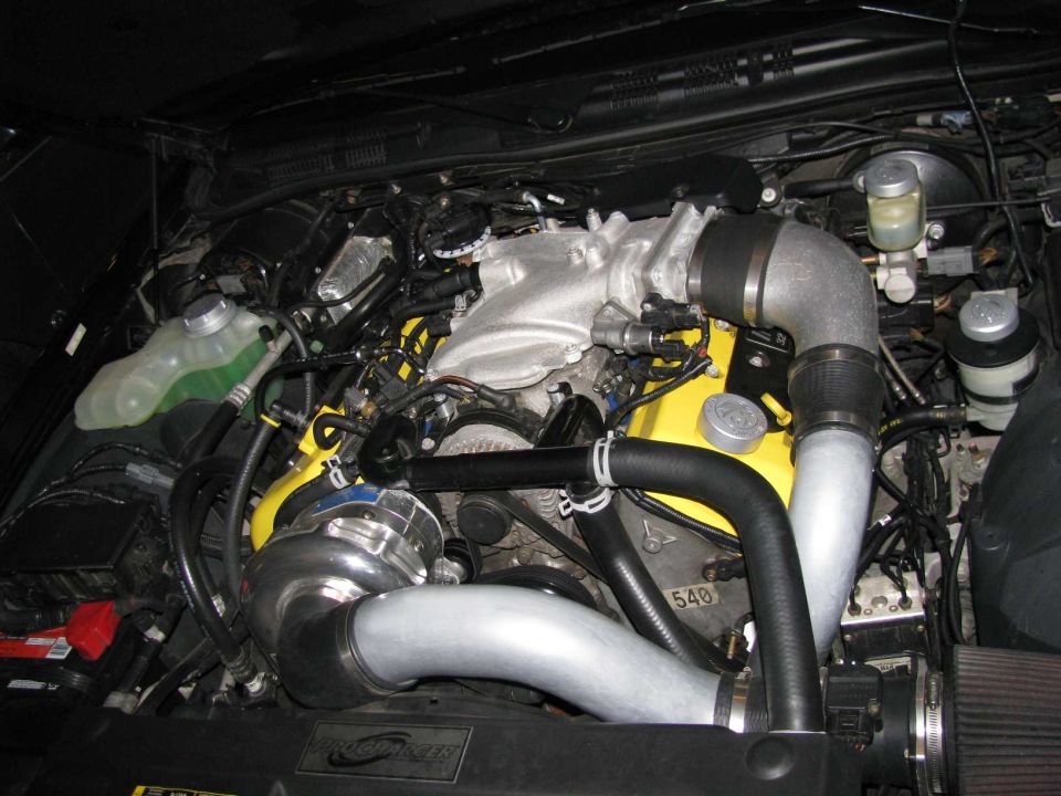 Engine bay with supercharger and yellow valve covers. Visible text '540'