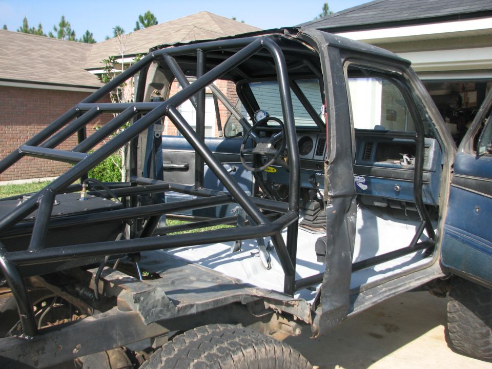 Roll cage inside a dark blue SUV, viewed from the passenger side. The interior is stripped down