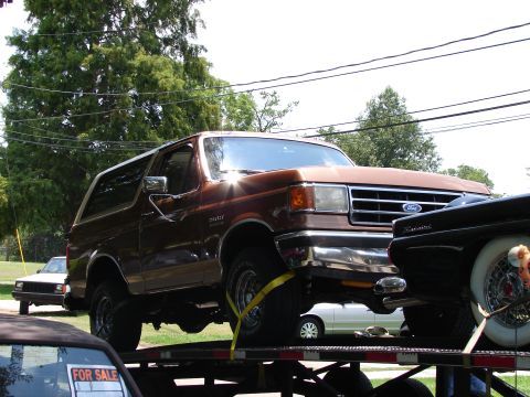 1989 Ford Bronco - A brown Ford Bronco is being transported on a car carrier, with a white car in the background.