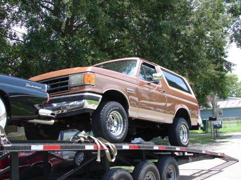1989 Ford Bronco - A brown Ford Bronco is loaded onto a car hauler, next to a black vehicle.