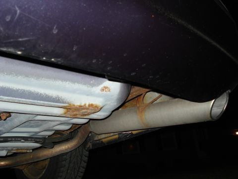 2000 Ford Crown Victoria - Close-up of a car's exhaust system, showing rust on the fuel tank and pipe.