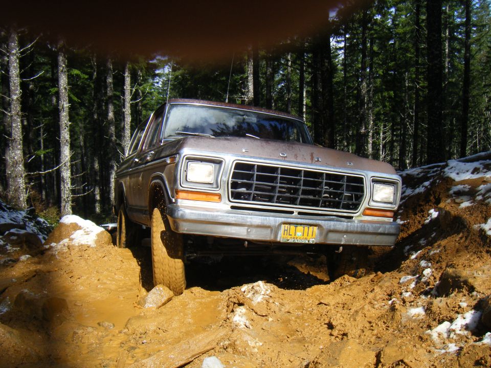 1978 Ford Bronco driving through mud on a wooded trail