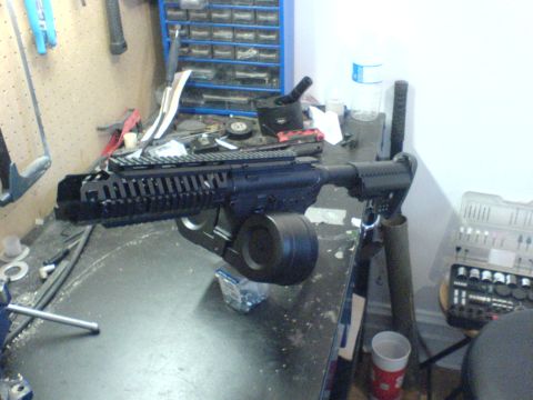 1985 Ford Bronco - An assault rifle with a drum magazine is displayed on a cluttered workbench.