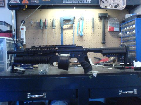 1985 Ford Bronco - A modified assault rifle with a large capacity drum magazine sits on a cluttered workbench.