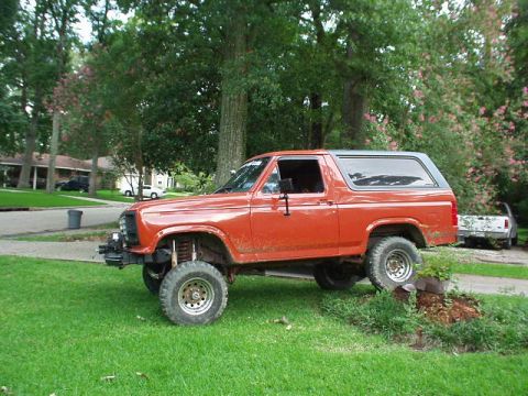 1983 Ford Bronco - Side view of an orange Ford Bronco parked on a grassy lawn.