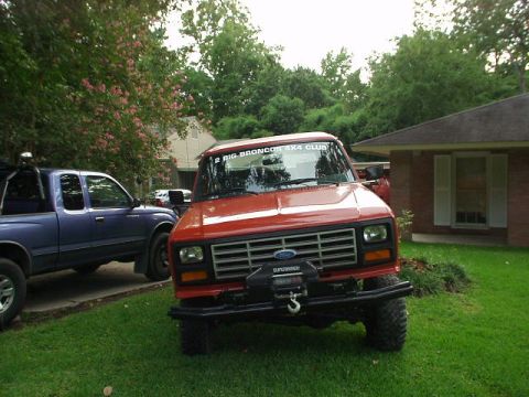 1983 Ford Bronco - A red Ford truck is parked on a lawn next to a blue pickup truck, with a house in the background.