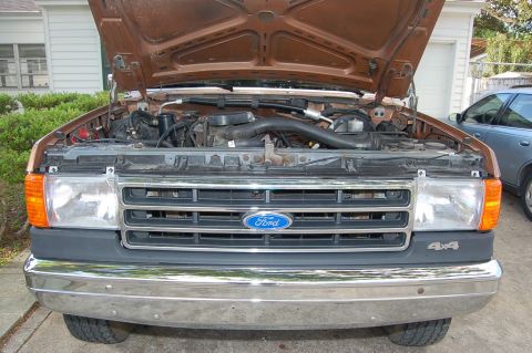 1989 Ford Bronco - The engine bay of a Ford truck is visible with the hood raised, revealing the engine and front grille.
