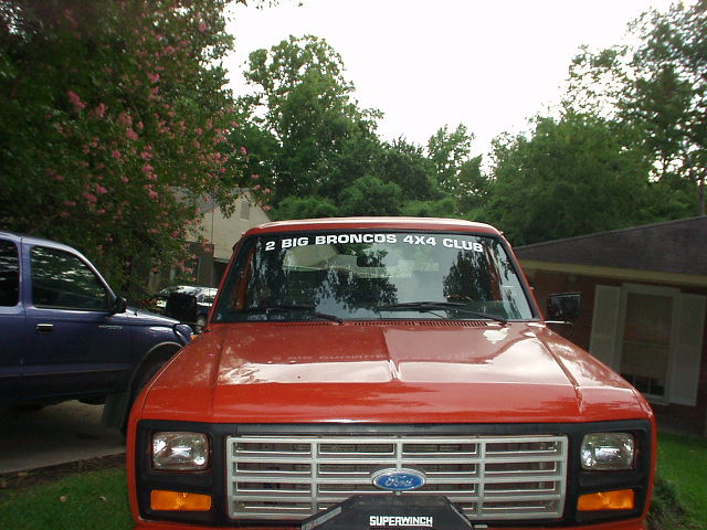 Red Ford truck front view, chrome grille, blue Ford emblem, "2 BIG BRONCOS 4X4 CLUB" sticker on windshield