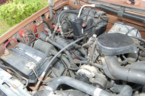 1989 Ford Bronco - Close-up view of the engine compartment, showing various hoses, wiring, and the battery.