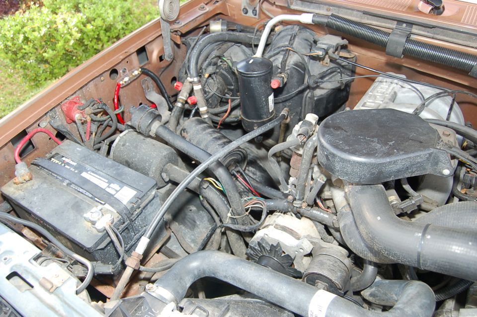 Engine bay of older truck with battery, air cleaner and AC components