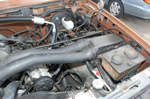 1989 Ford Bronco - Engine bay components including hoses, brake fluid reservoir, and air intake system. A second vehicle is visible in the background.
