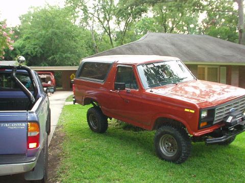 1983 Ford Bronco - A red 1983 Ford Bronco is parked on the grass next to a blue pickup truck.