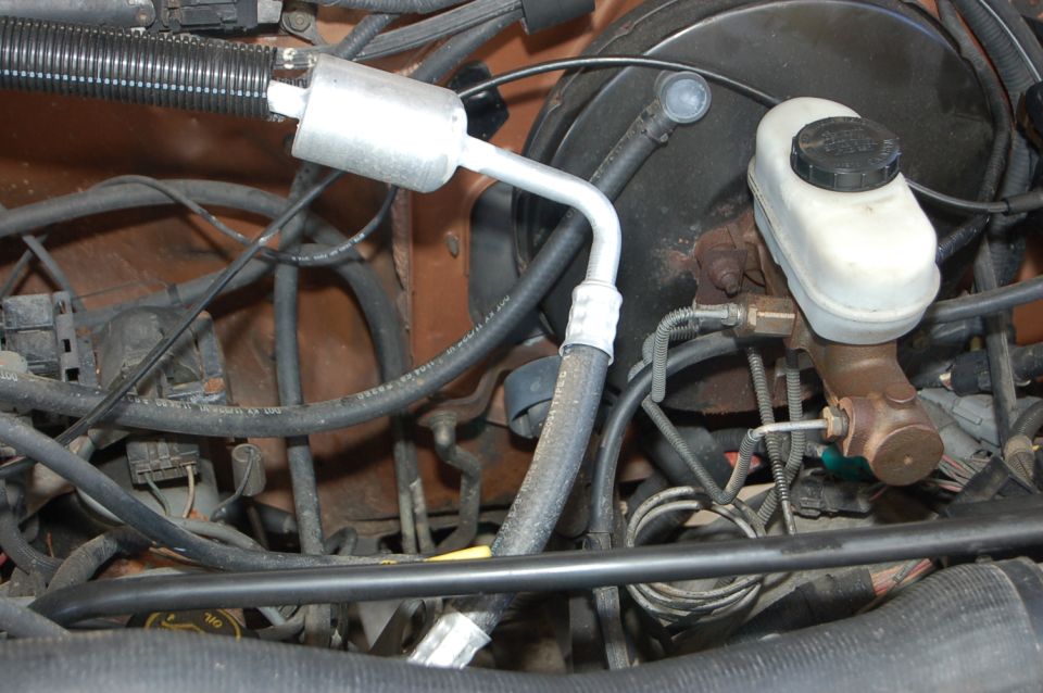 Engine bay with brake fluid reservoir, hoses, and wiring. Orange painted firewall visible
