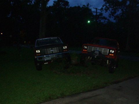 1983 Ford Bronco - Two trucks are parked on a grassy area at night, with trees in the background.