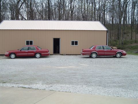 1999 Mercury Grand Marquis - Two red sedans are parked outside a building, with one on the left and another on the right.