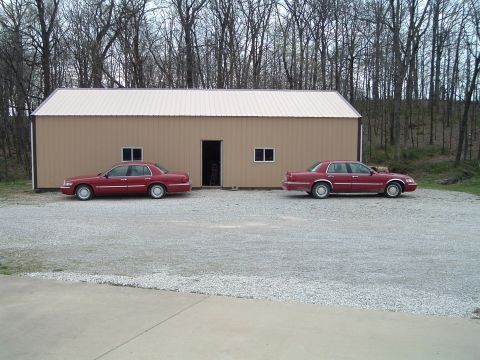 1999 Mercury Grand Marquis - Two red 1999 Mercury Grand Marquis sedans are parked in front of a tan building.