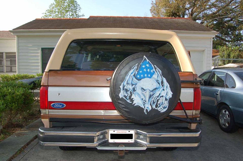 1989 Ford Bronco rear bumper, taillights, and spare tire cover with eagle graphic. Another car is parked to the right