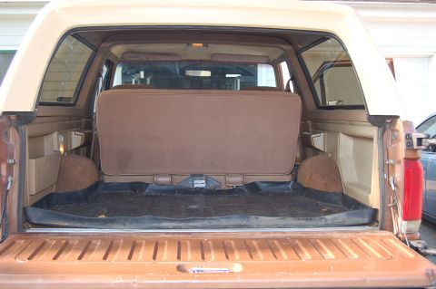 1989 Ford Bronco - The cargo area of a brown SUV shows a folded rear seat and a rubber floor mat, with side storage compartments visible.
