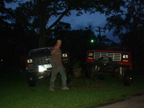 1983 Ford Bronco - Two pickup trucks are parked on a grassy area with trees in the background at twilight.