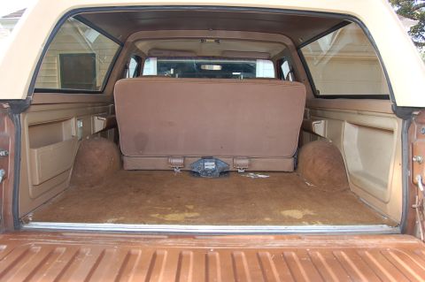 1989 Ford Bronco - The cargo area of a vehicle features a folded brown rear seat and a visible trailer hitch.