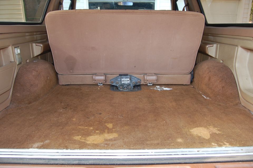 Rear cargo area with folded-down seat and carpeted floor. Visible hitch mechanism in center