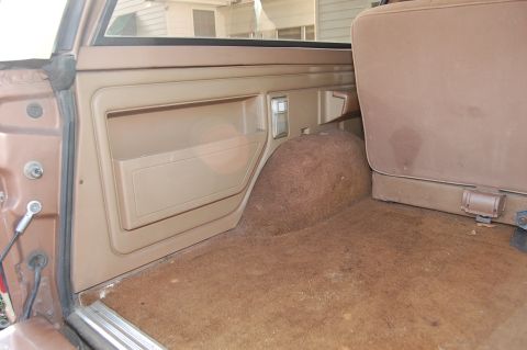 1989 Ford Bronco - The rear interior of an older SUV shows a tan door panel and carpeted cargo space.