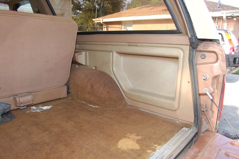 1989 Ford Bronco - The interior cargo area of a brown SUV shows tan panels and carpet, with a partial view of another vehicle outside.