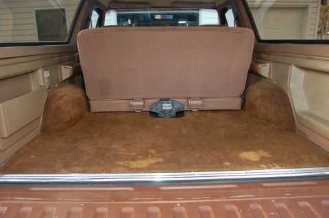 1989 Ford Bronco - The cargo area of an SUV shows a folded rear seat and a trailer hitch receiver, with carpeted wheel wells.