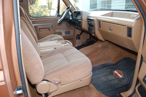 1989 Ford Bronco - The interior features tan bucket seats, a tan dashboard with wood trim accents, and black floor mats.