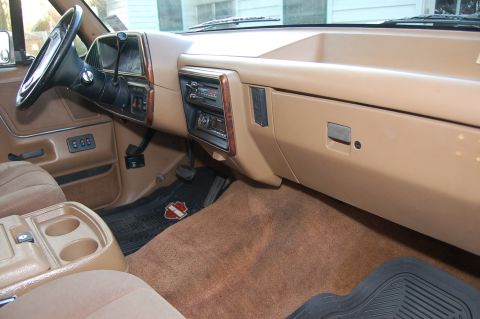 1989 Ford Bronco - The interior of a vehicle features a tan dashboard, steering wheel, and seats with a center console and radio.