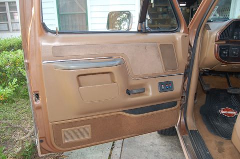 1989 Ford Bronco - The interior door panel of a vehicle shows brown upholstery and a Harley-Davidson floor mat on the passenger side.