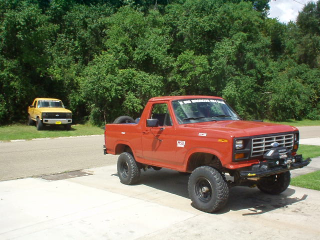 red Ford Bronco with aftermarket bumper and winch, yellow Ford pickup in background