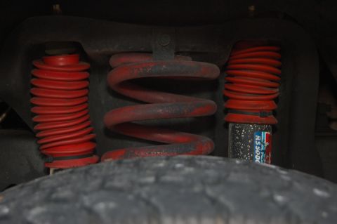 1989 Ford Bronco - Close-up view of red coil springs and shock absorbers with red boots, part of a vehicle's suspension system.
