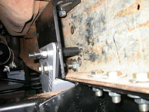1990 Ford Bronco - Close-up underbody shot of a bolt-on steel bracket sandwiched against a rusty boxed frame rail, secured with zinc-plated bolts, washers and…