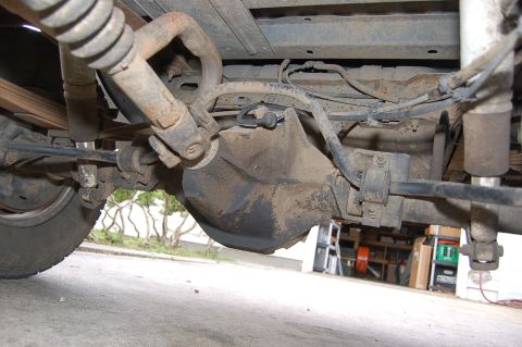 1989 Ford Bronco - The underside of a vehicle shows its rear axle assembly, leaf springs, and shock absorbers, with some signs of wear and tear.