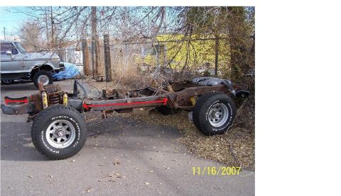 1991 Ford Bronco - A rusted vehicle frame sits on the ground with tires, another vehicle is visible in the background.