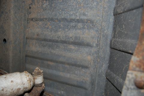 1989 Ford Bronco - The underside of a vehicle shows a section of ribbed metal and a pipe, with visible rust and dirt.