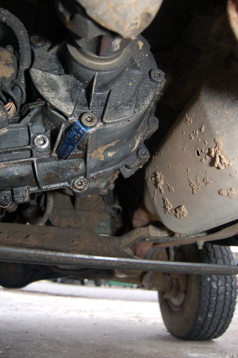1989 Ford Bronco - Close-up of the transfer case and exhaust system from beneath a vehicle.