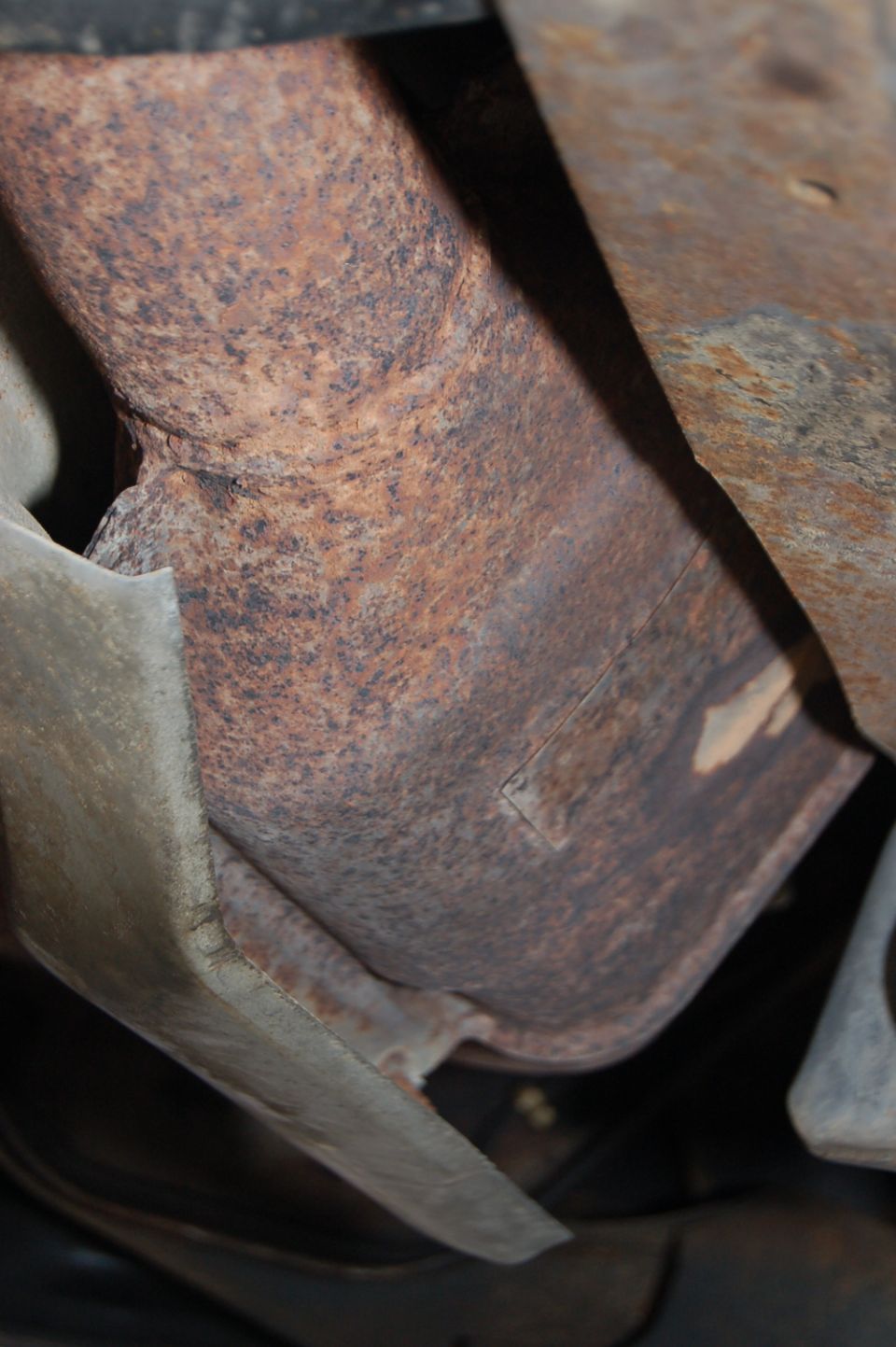 Close-up of a rusted exhaust pipe and undercarriage parts, likely from a vehicle