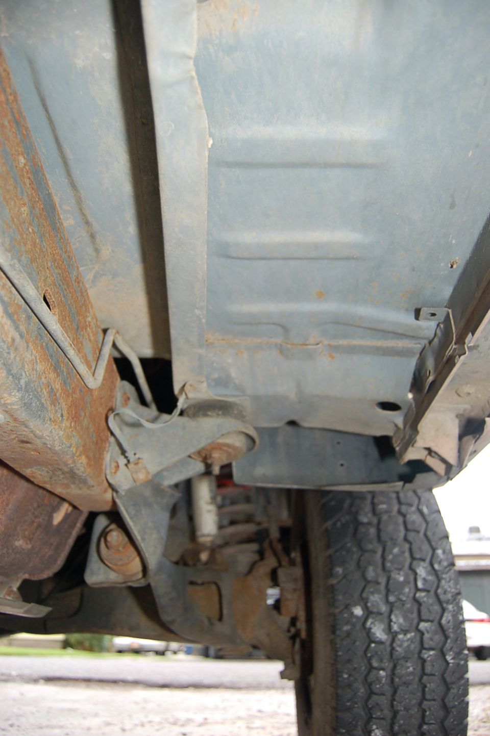 Underside of a vehicle showing rusted frame, suspension components, and a tire